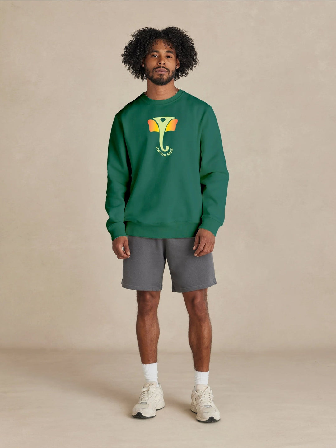 Man wearing a green sweatshirt with a logo, gray shorts, and white sneakers on a beige background